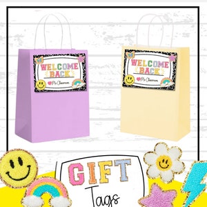 May include: Two gift bags with colourful "Welcome Back" tags. The tags have a rainbow, a heart, a smiley face, and a butterfly. The bags are purple and yellow. The text below the tags says "Mr. Classroom".
