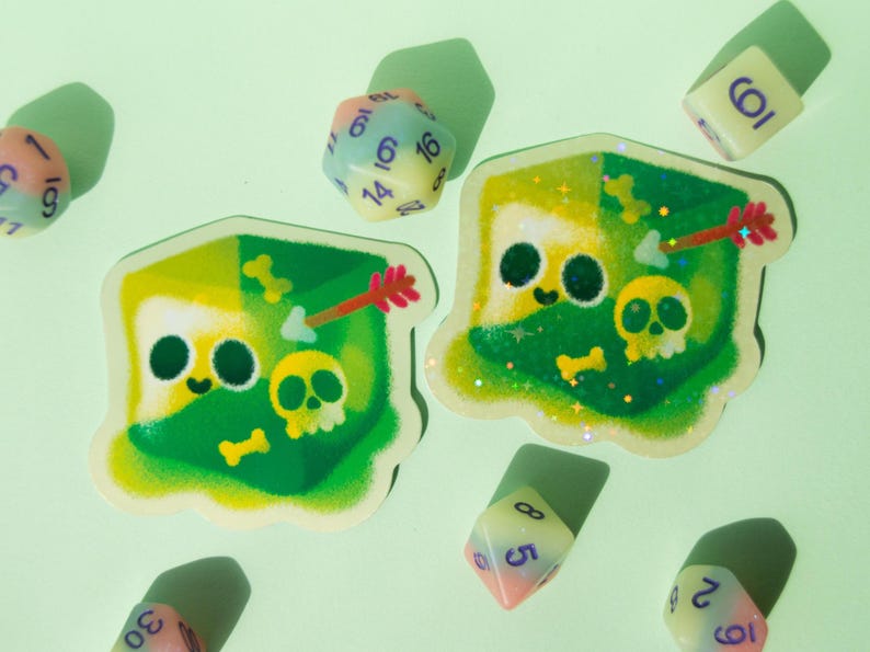 May include: Two green and white dice stickers with glitter and a cartoon skull and arrow design. The stickers are on a light green background with other dice.