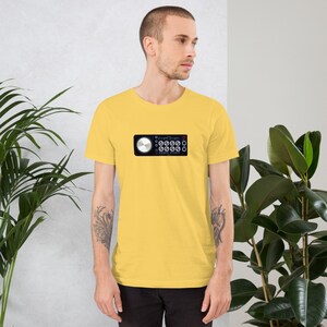 May include: Yellow short-sleeve t-shirt featuring a graphic of a black audio control panel with a silver dial and blue lights. The shirt is made of a soft, comfortable material.