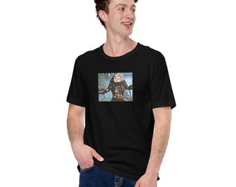 May include: A black short-sleeved t-shirt featuring a rectangular graphic print on the chest. The graphic depicts a detailed, dark-toned creature with textured armour and a menacing expression, set against a blurred, natural forest background.