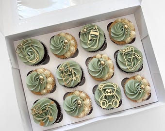 Può includere: Una scatola di 12 cupcake verdi e dorati decorati con topper a tema baby. I topper includono un biberon, una tutina, un orsacchiotto, un'impronta di piede e le parole "Oh Baby".
