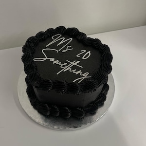 May include: A black cake with black frosting and a silver inscription that reads "Mrs. 20 Something".
