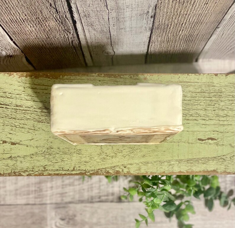 May include: A small, white ceramic planter with a brown and beige patterned base. The planter is sitting on a wooden surface.