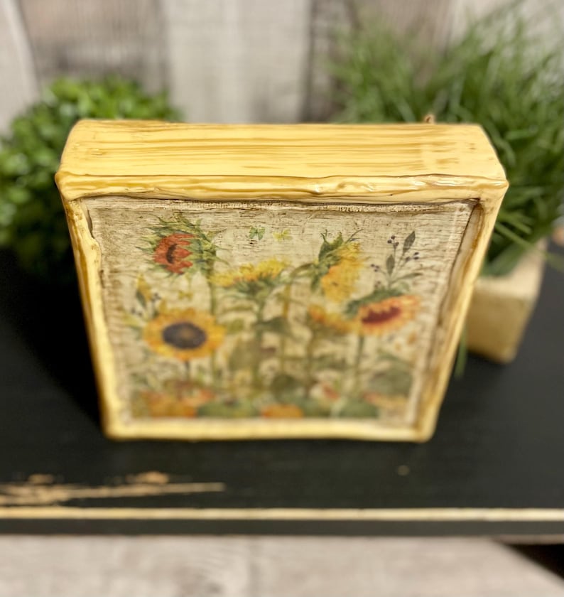 Framed vintage sunflower canvas art with beeswax textured finish, featuring rustic yellow sunflowers and wildflowers in farmhouse style canvas frame.