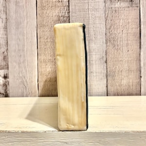 May include: A rectangular, off-white ceramic object with a dark blue edge. The object has a textured surface with vertical lines. The background is a light-colored wooden wall.