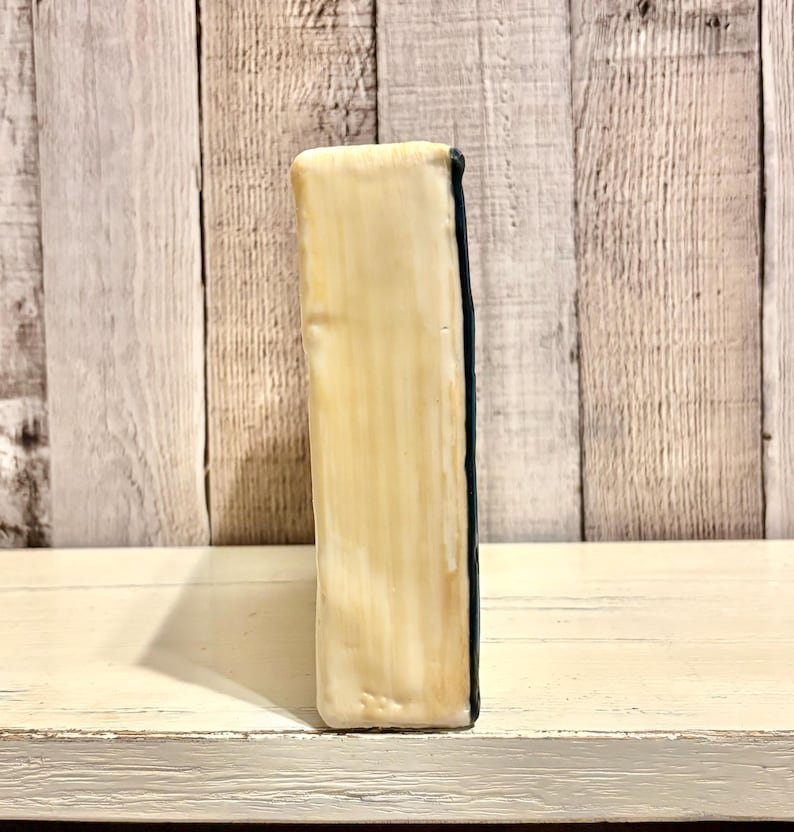 May include: A rectangular, off-white ceramic object with a dark blue edge. The object has a textured surface with vertical lines. The background is a light-colored wooden wall.