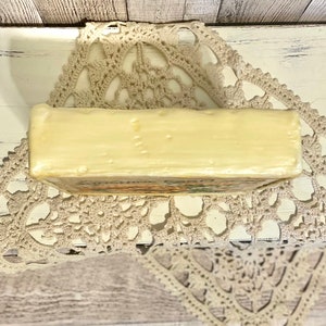 May include: A rectangular bar of ivory-colored soap with a floral design on the bottom. The soap is sitting on a white crocheted doily.