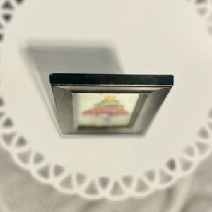 May include: A framed artwork featuring a colorful mushroom with a crown on top. The frame is black with a distressed finish.