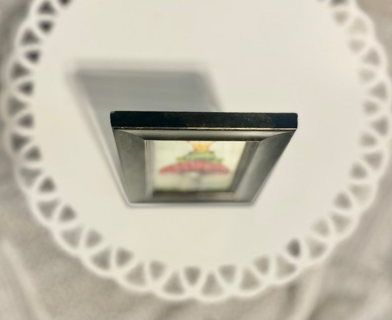 May include: A framed artwork featuring a colorful mushroom with a crown on top. The frame is black with a distressed finish.