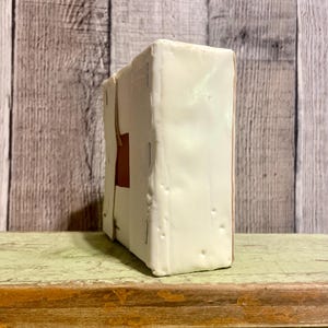 May include: A white box with a brown rectangle on the front. The box is sitting on a green surface.