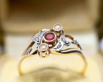 May include: A gold ring with a red gemstone and two white pearls set in a delicate, swirling design.