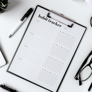 May include: A black and white habit tracker with a clipboard style binding. The tracker has four weeks and a month section with days of the week labeled. The text "habit tracker" is at the top of the page.