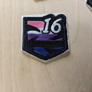 May include: A black and white embroidered patch with a purple, white, and pink stripe design. The number "16" is embroidered in white on the patch.
