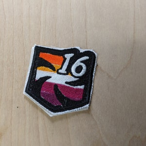 May include: A white, black, orange, and purple embroidered patch with a palm tree and the number 16.