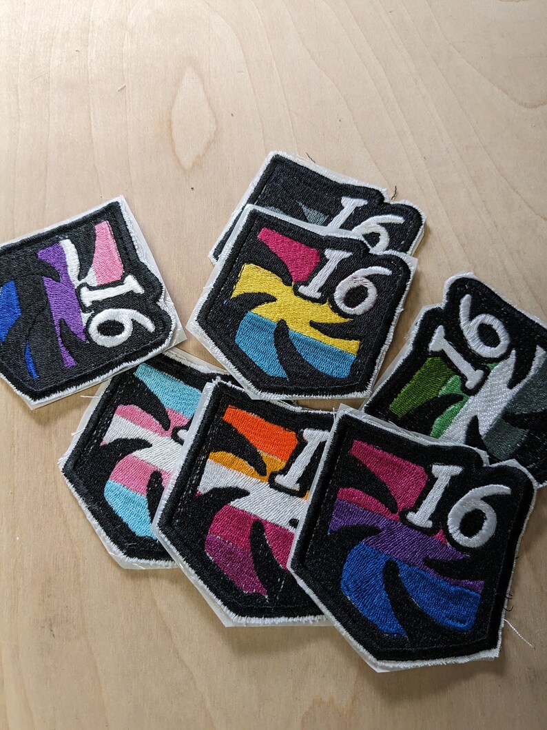 以下が含まれることがあります： ヤシの木のデザインと数字の16が刺繍された8つのパッチのセット。各パッチは、トランスジェンダーのプライドフラッグの異なる色の組み合わせを特徴としています。