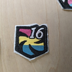 May include: A black and white embroidered patch with a palm tree and the number 16. The palm tree is colored with pink, yellow, and blue stripes.