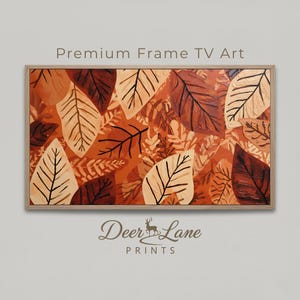 Może przedstawiać: Oprawiona grafika przedstawiająca abstrakcyjny wzór jesiennych liści w odcieniach brązu, beżu i pomarańczy. Grafika oznaczona jest jako "Premium Frame TV Art" i zawiera logo Deer Lane Prints.