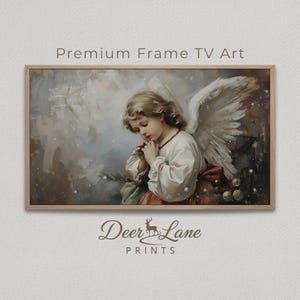Puede incluir: Impresión enmarcada con una pintura vintage de un joven ángel con cabello rubio, alas blancas y una túnica blanca con una faja roja. El texto "Premium Frame TV Art" está en la parte superior y "Deer Lane Prints" en la inferior.