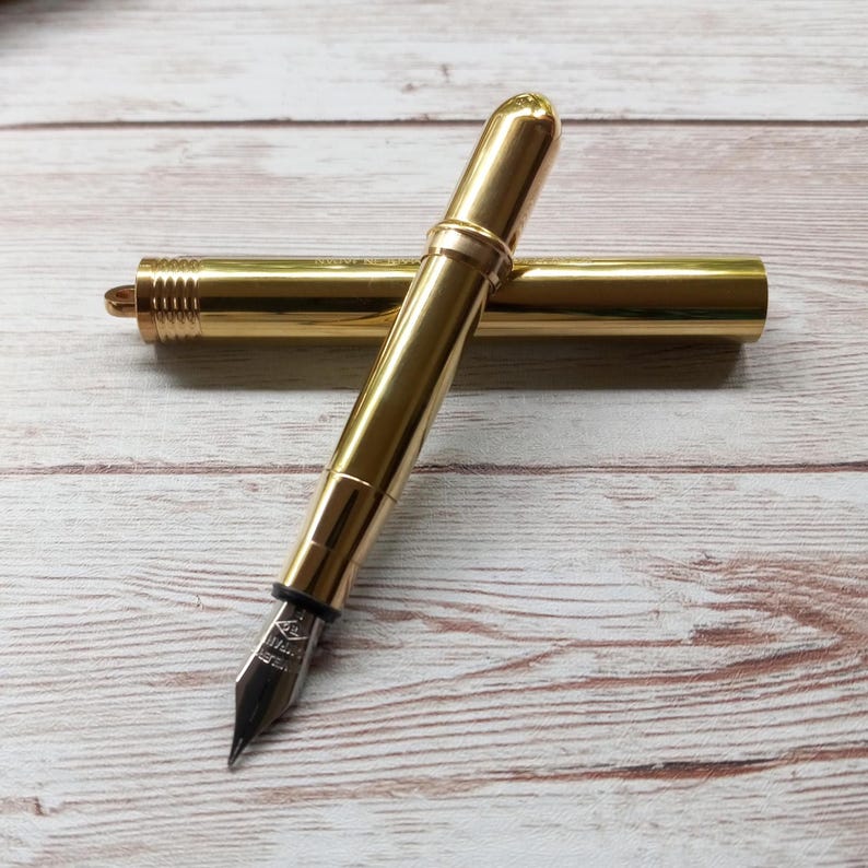 May include: A white ceramic mug with a black handle and the text "But First, Coffee" in a handwritten style. The mug is on a white surface. The mug is approximately 10 cm tall.