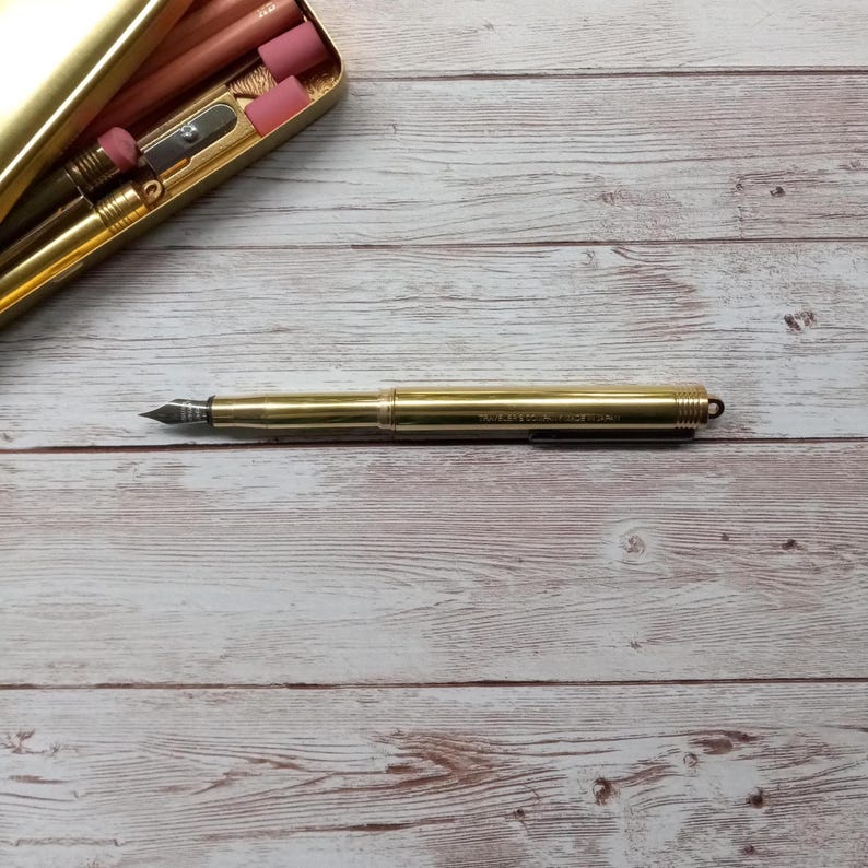 May include: A white ceramic mug with a black handle and the text "But First, Coffee" in a bold, black font. The mug is set against a blurred background, suggesting a cosy setting.