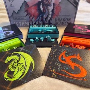 Könnte beinhalten: Ein Brettspiel-Set mit Komponenten zum Thema Drachen. Das Spiel enthält Schachteln in verschiedenen Farben, wie Schwarz, Grün und Orange, mit Drachenillustrationen und Spielsteinen. Das Box-Art zeigt eine Drachenillustration.