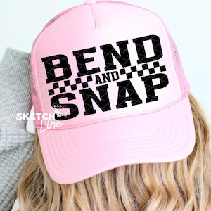 Puede incluir: Gorra rosa claro con la frase "BEND AND SNAP" en letras negras. La gorra tiene una parte trasera de malla y una visera curvada. El texto está sobre un pequeño patrón de cuadros.