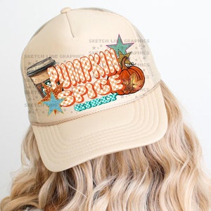May include: A beige trucker hat with a mesh back. The front of the hat features a colorful graphic with the text "Pumpkin Spice" and a coffee cup, pumpkin, and stars.