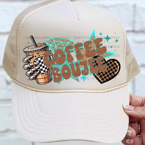 Puede incluir: Una gorra de camionero de malla beige con un gráfico marrón y blanco de una taza de café con el texto "Coffee Bestie" en una fuente retro. El gráfico también incluye un corazón con un patrón a cuadros.