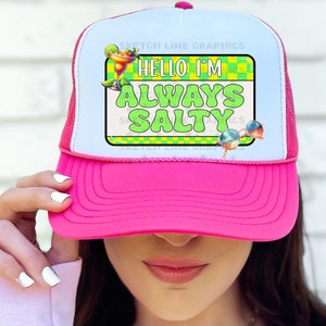 May include: Pink trucker hat with a white mesh back. The hat has a green and yellow graphic with the text "Hello I'm Always Salty".