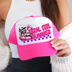 May include: A pink and white trucker hat with the text "FERAL GIRL SUMMER" in purple and pink. The hat features a graphic of a raccoon wearing sunglasses and a flamingo floatie. The hat has a mesh back.