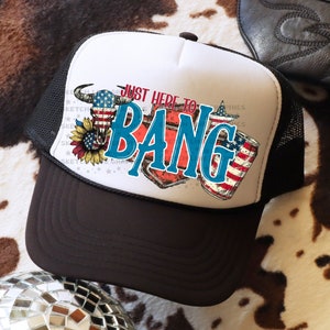 May include: A white and black trucker hat with a red, white, and blue design. The hat features a bull skull with a sunflower and the text "Just Here To Bang".