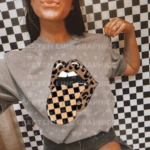 May include: A gray t-shirt with a graphic of a leopard print mouth with a checkered tongue. The shirt has a distressed look and is decorated with small white stars.