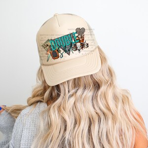 May include: A beige trucker hat with a turquoise and brown graphic that says "Double Shot" and features a heart, playing cards, and other designs.
