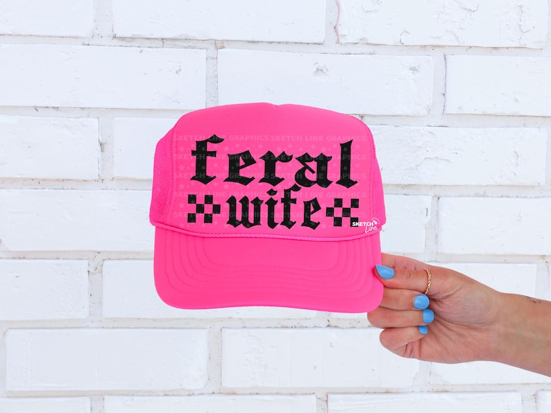 May include: A bright pink trucker hat with the words "feral wife" in black gothic lettering. The hat has a mesh back and a curved brim. The text is centered on the front of the hat.