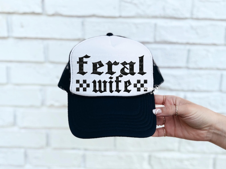 May include: Black and white trucker hat with the words "feral wife" in a gothic font. The hat has a white front panel with the text and a black mesh back. The brim is black.