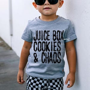 May include: A young person wearing a grey t-shirt with the text "Juice Box Cookies & Chaos" printed in black. The person is wearing black and white checkered pants.