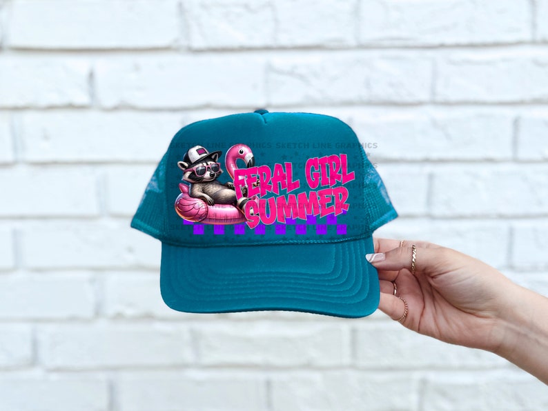 Puede incluir: Gorra de camionero turquesa con un dise&ntilde;o de un mapache con gafas de sol en un flotador de flamenco rosa. El texto "FERAL GIRL SUMMER" es rosa y morado. Un divertido accesorio de verano.