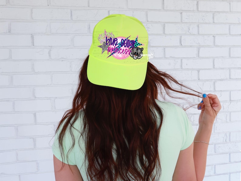 May include: A neon yellow baseball cap with a black and white tiger graphic and the text "Blue Collar Princess" in colorful letters.