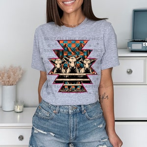 May include: A gray t-shirt with a graphic of three cows in front of a fence with a mountain and sunset scene behind them. The graphic is in a geometric pattern with pink, orange, blue, and green colors.