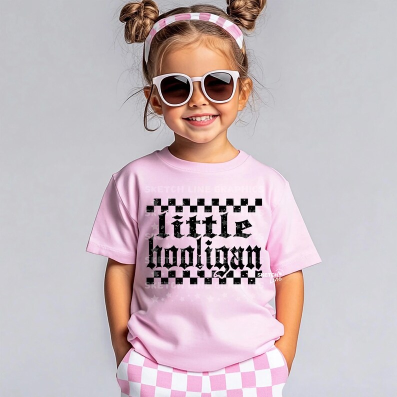 K&ouml;nnte beinhalten: Ein pinkfarbenes T-Shirt mit einem schwarzen Karomuster und dem Text "little hooligan" in gotischer Schrift.