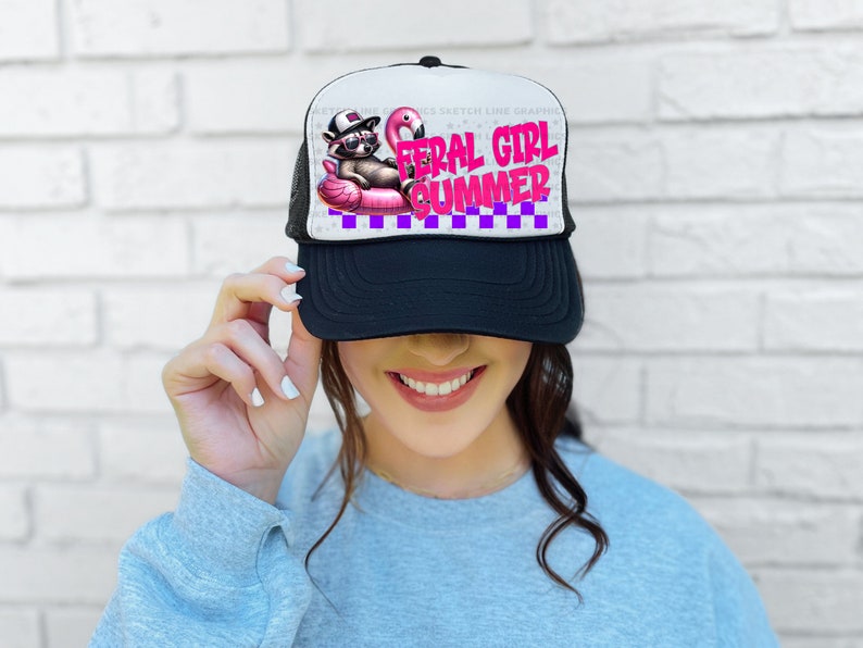 Puede incluir: Gorra de camionero en blanco y negro con el texto "FERAL GIRL SUMMER" en rosa y morado. La gorra presenta un gr&aacute;fico de un mapache con gafas de sol y sombrero, flotando en un flotador de flamenco rosa.