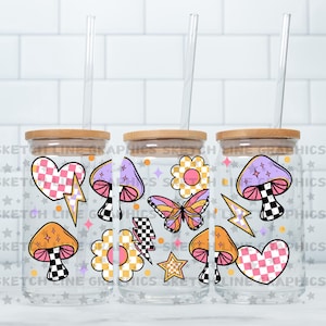 May include: Three clear glass tumblers with bamboo lids and reusable straws. Each tumbler features a different design with a psychedelic theme, including mushrooms, butterflies, hearts, and stars.