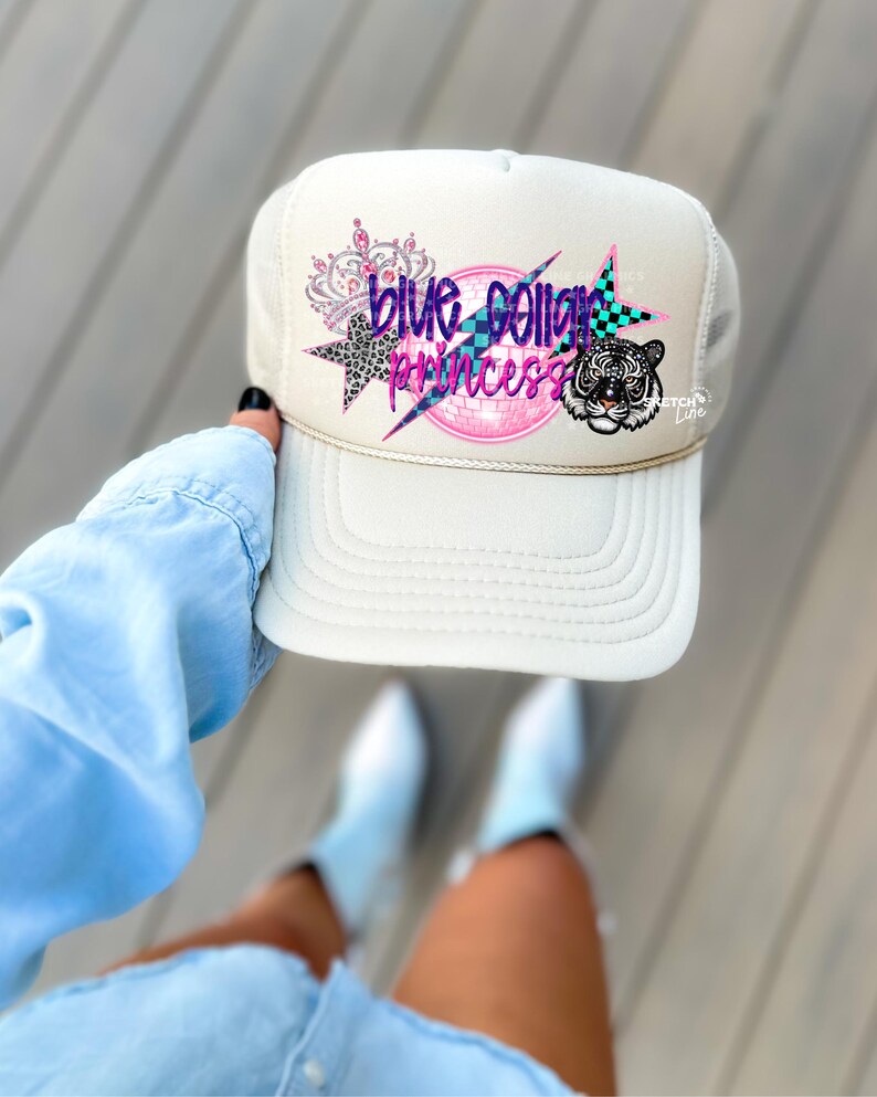 May include: A white trucker hat with a blue, pink, and black design that says "Blue Collar Princess". The design also includes a crown, a star, and a tiger.