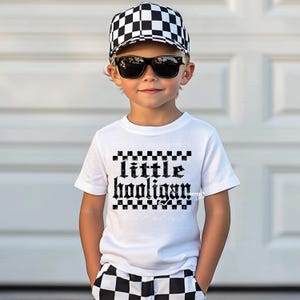 K&ouml;nnte beinhalten: Ein wei&szlig;es T-Shirt mit einem schwarz-wei&szlig;en Karomuster und dem Text "little hooligan" in Schwarz. Das Shirt wird von einem Kind getragen, das eine schwarz-wei&szlig;e karierte M&uuml;tze und eine schwarze Sonnenbrille tr&auml;gt.