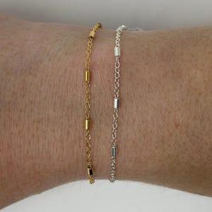 May include: Two delicate chain bracelets, one gold and one silver, with small cylindrical beads spaced along the chains.