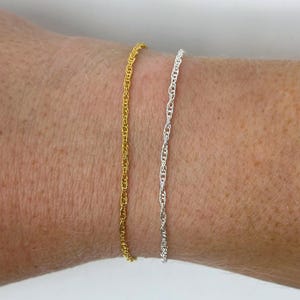 May include: Two delicate chain bracelets, one gold and one silver, worn on a wrist.