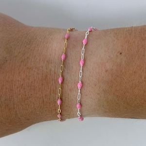 May include: Two delicate bracelets with pink beads. One bracelet has a gold chain, and the other has a silver chain. The bracelets are worn on a wrist, showcasing the jewelry's design and color.