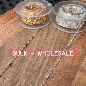 May include: Two spools of chain, one gold and one silver, with the text "BULK - WHOLESALE" on a wooden surface.