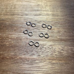May include: Five silver infinity symbol charms on a wooden surface.