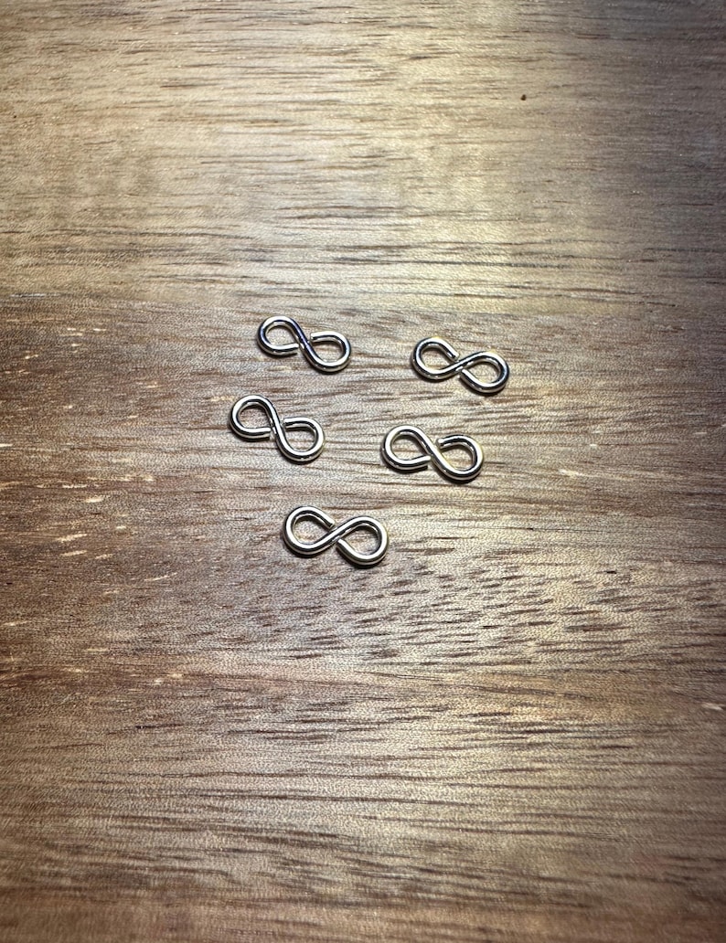 May include: Five silver infinity symbol charms on a wooden surface.